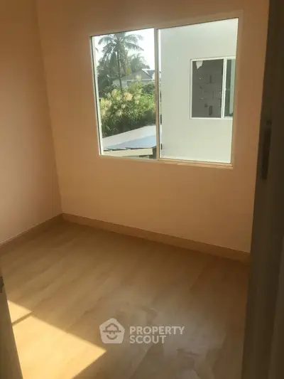 Bright empty room with wooden flooring and large window overlooking greenery.