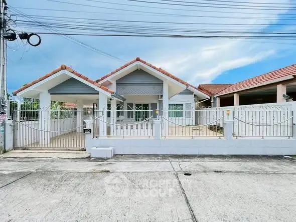 Charming single-story house with gated entrance and tiled roof in a serene neighborhood.