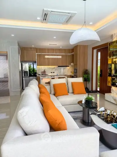 Luxurious modern living room with open kitchen, featuring stylish decor and vibrant orange accents.