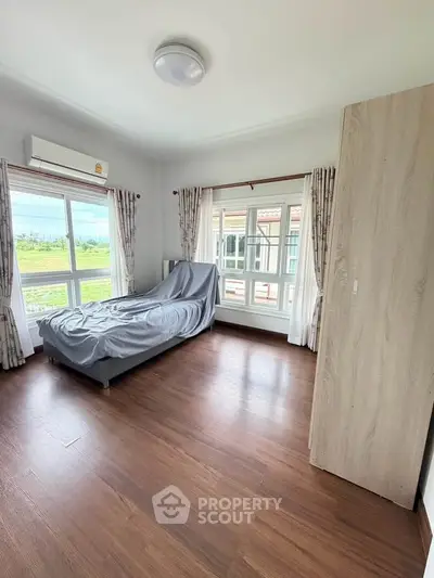 Spacious bedroom with large windows and wooden flooring, offering a serene view.