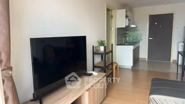Modern living room with sleek TV and compact kitchen in open layout apartment.