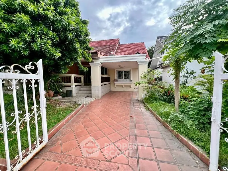 Charming suburban home with red-tiled roof and spacious driveway, surrounded by lush greenery.