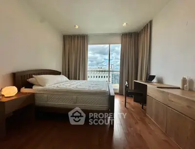 Spacious bedroom with wooden flooring and city view, featuring a cozy bed and modern furniture.