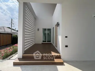 Modern home entrance with sleek design and wooden steps, featuring a stylish lattice wall and glass door.
