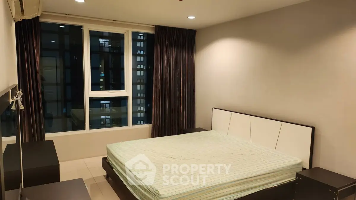 Spacious bedroom with large window and modern furnishings in a high-rise apartment.
