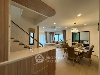 Spacious modern living room with open dining area and elegant staircase, featuring chic decor and ample natural light.