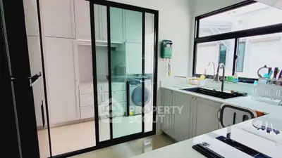 Modern kitchen with sleek design and laundry area, featuring large windows and ample storage.