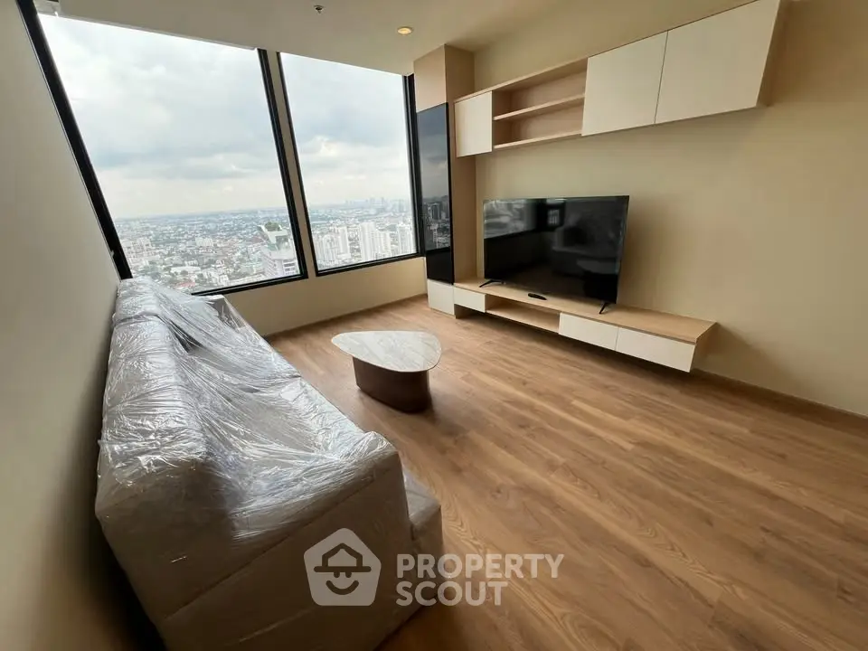 Modern living room with large windows offering stunning city views, featuring a sleek TV setup and cozy seating.