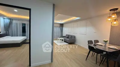 Modern open-plan living room with dining area and bedroom, featuring stylish lighting and wooden flooring.