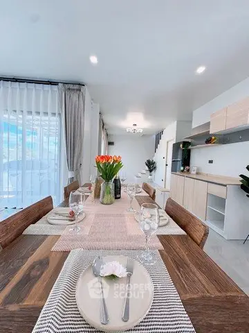 Elegant dining area with wooden table, modern decor, and open kitchen layout in a bright, airy apartment.