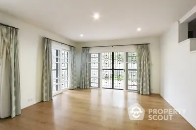 Spacious and bright living room with polished hardwood floors, large windows with French doors leading to a balcony, and elegant light fixtures.