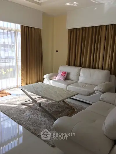 Spacious living room with elegant white sofas and natural light through large windows.