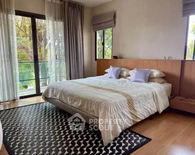 Spacious bedroom with large windows and balcony access, featuring elegant decor and natural light.