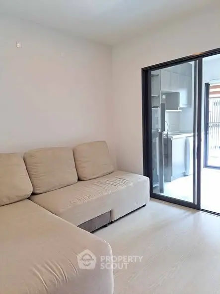 Modern living room with beige sofa and sliding glass doors leading to kitchen area.