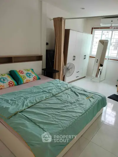 Cozy bedroom with modern decor, featuring a comfortable bed, wardrobe, and natural light from large window.