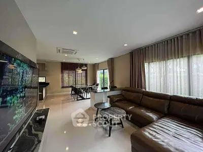 Spacious modern living room with leather sofa and open dining area, featuring large windows and elegant decor.