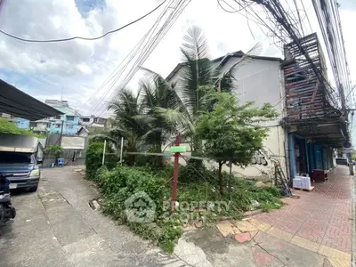 Urban corner lot with potential for development, featuring lush greenery and street access.