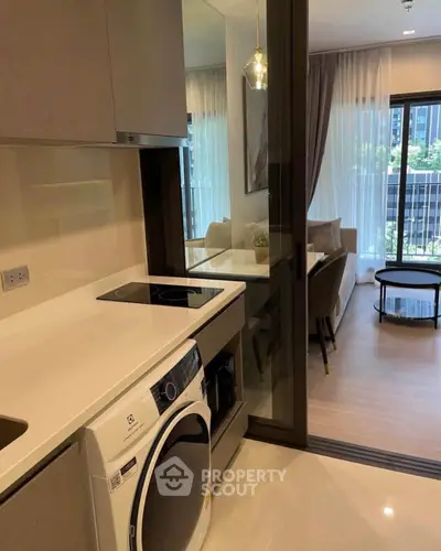 Modern apartment with sleek kitchen and cozy living area, featuring a washing machine and large windows.