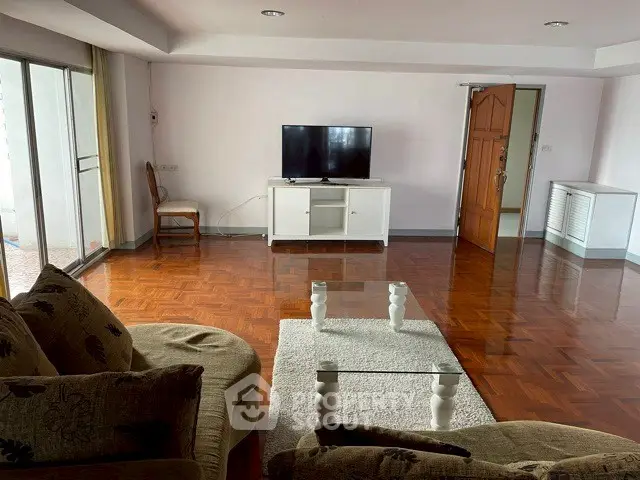 Spacious living room with hardwood floors, modern furniture, and large TV, perfect for relaxation.