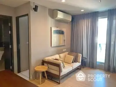 Cozy living room with modern furniture, wooden flooring, and elegant drapery, leading to a sunlit balcony.