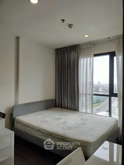 Modern bedroom with large window offering city view, featuring a comfortable bed and stylish decor.