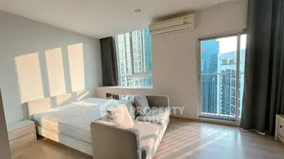Modern bedroom with large windows and city view, featuring a cozy bed and stylish sofa.