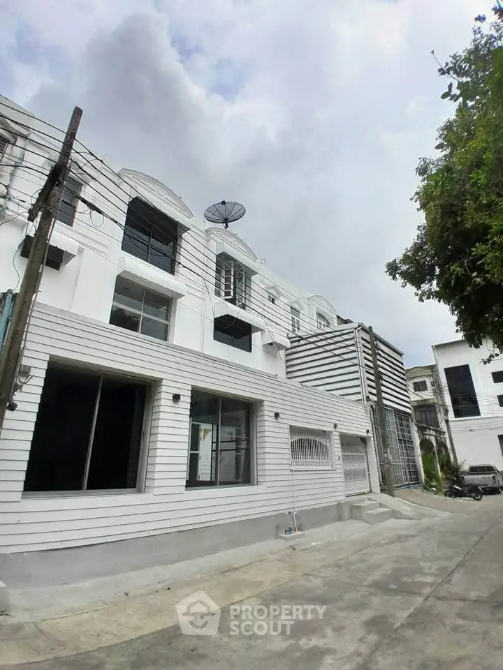 Modern white building exterior with large windows and satellite dish under cloudy sky.