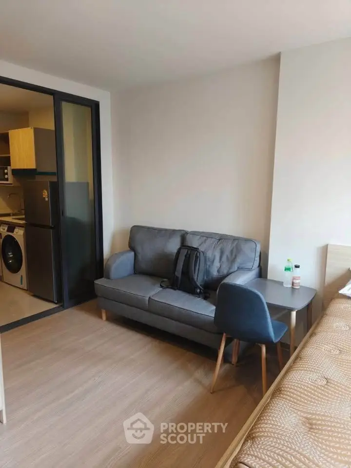 Modern studio apartment with cozy living area and compact kitchen featuring washing machine and fridge.