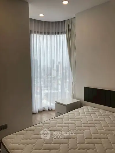 Modern bedroom with large window and city view, featuring a comfortable mattress and sleek design.