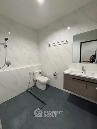 Modern bathroom with sleek fixtures and marble walls, featuring a spacious shower area and elegant vanity.