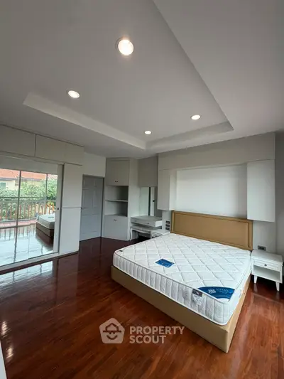 Spacious bedroom with hardwood floors and balcony access in modern home.