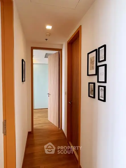 Elegant hallway with wooden flooring and framed art, leading to a bright room.