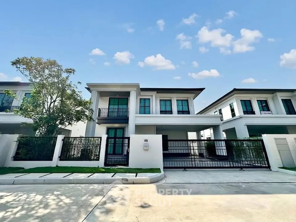 Modern two-story house with gated driveway and lush greenery under a clear blue sky.