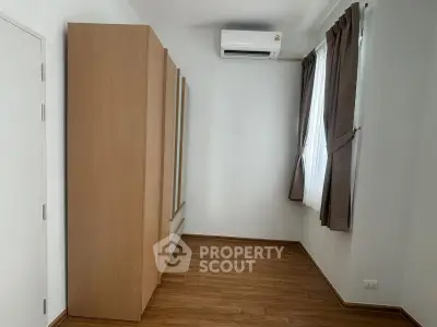 Spacious bedroom with wooden flooring and large wardrobe, featuring natural light from window.