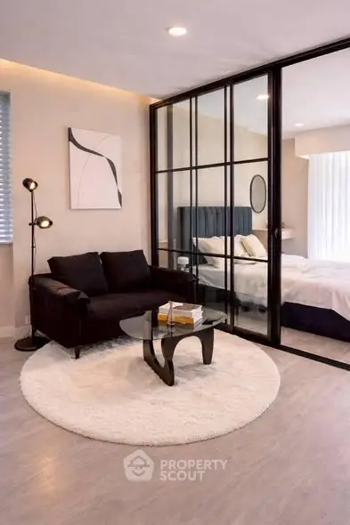 Modern living room with glass partition leading to a cozy bedroom, featuring elegant decor and ambient lighting.