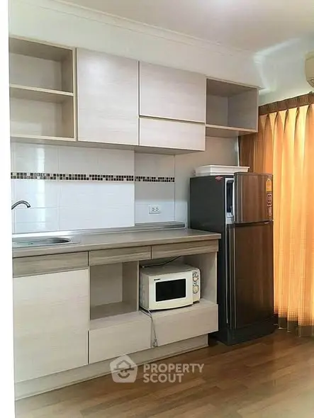 Modern kitchen with sleek cabinetry, microwave, and fridge in a cozy apartment setting.