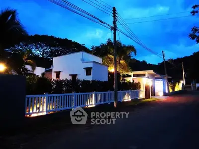 Charming white house with lush greenery and ambient lighting at dusk, offering serene and inviting curb appeal.