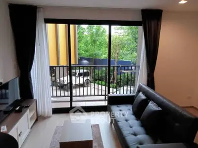 Modern living room with large window and balcony view, featuring sleek furniture and natural light.