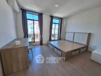 Spacious bedroom with modern wooden furniture and large windows offering natural light.