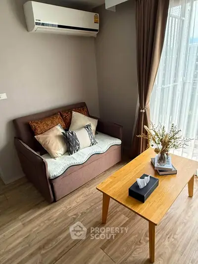Cozy living room with air conditioning and natural light, featuring a stylish sofa and wooden coffee table.