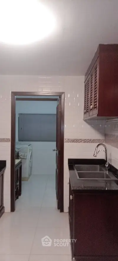 Modern kitchen with dark wood cabinets and adjacent laundry area, featuring sleek countertops and tiled walls.