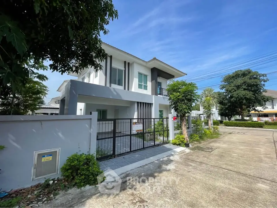 Modern two-story house with gated entrance and lush greenery in a serene neighborhood.