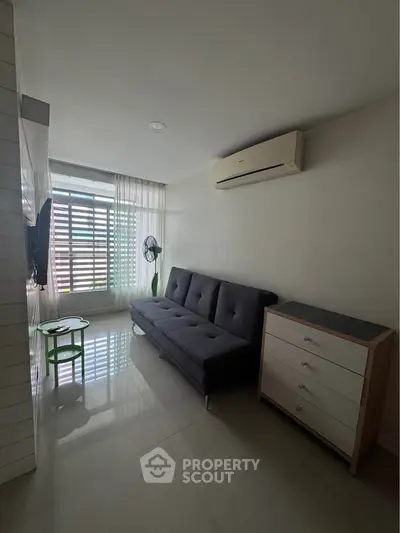 Modern living room with sleek sofa, air conditioning, and natural light from large window.