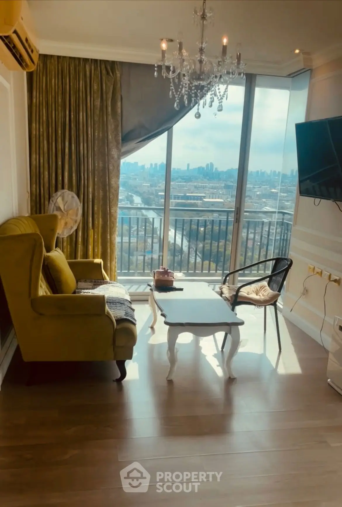 Elegant living room with chandelier and stunning city view from large windows.