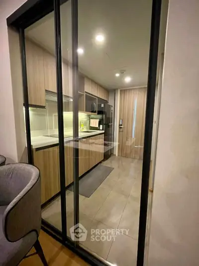 Modern kitchen with sleek wooden cabinetry and glass sliding doors in a contemporary apartment.