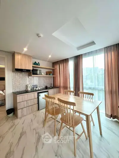 Modern kitchen with dining area, featuring wooden cabinets and large windows for natural light.
