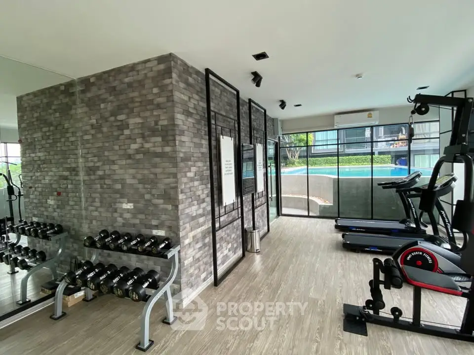 Modern gym with exercise equipment and pool view in luxury apartment complex.