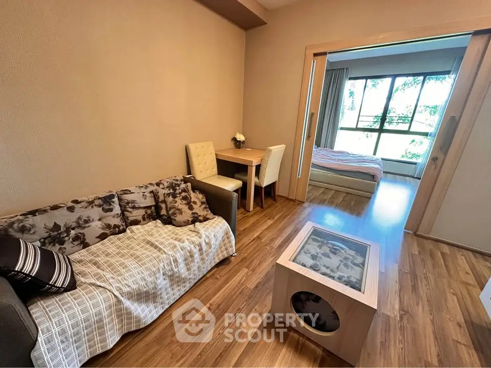 Cozy living room with wooden flooring and a view into a bright bedroom, perfect for modern living.