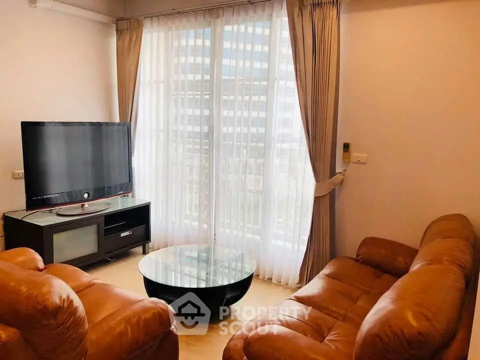Spacious living room with leather sofas and large TV, featuring floor-to-ceiling windows for natural light.
