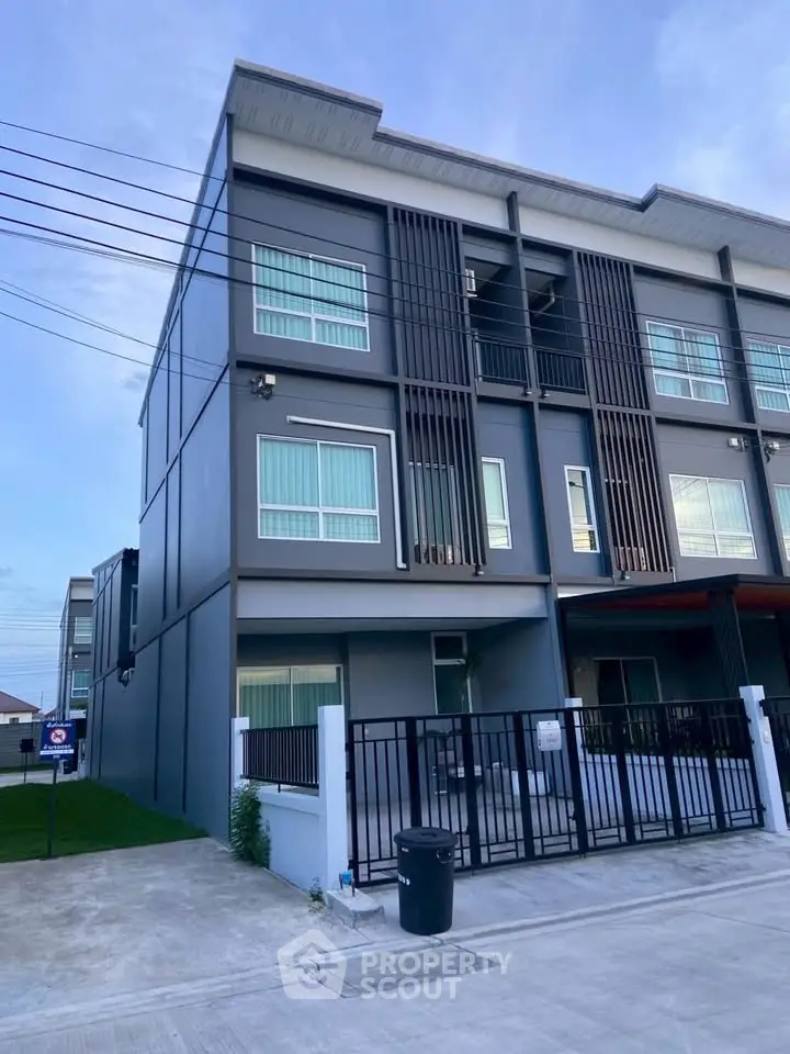 Modern three-story townhouse with sleek design and gated entrance in a suburban neighborhood.